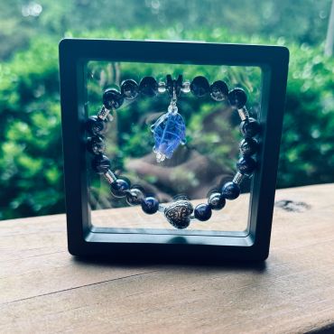 A beaded bracelet with a blue pendant displayed in a clear black frame.