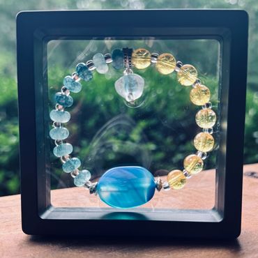 Colorful beaded bracelet displayed in a black frame with a green outdoor background.