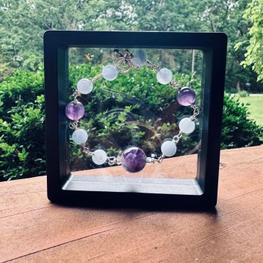 A beaded bracelet displayed in a black frame with a garden background.