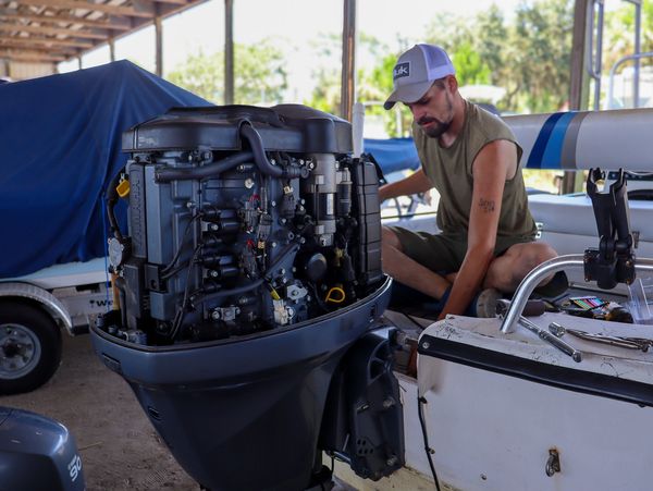 Man repairing an outboard motor on a boat in a covered dock.