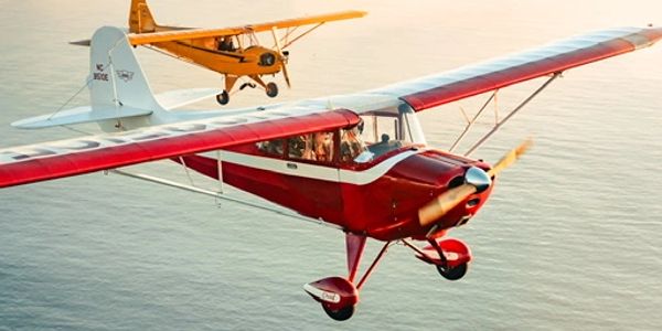 Two small vintage airplanes flying over water.