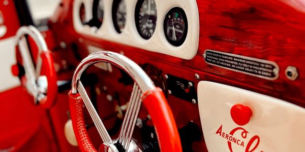 Close-up of a classic car's red and white dashboard and steering wheel.
