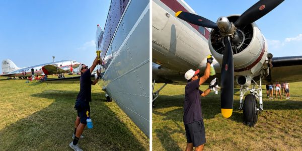 Man cleaning an airplane at an airfield on a sunny day.