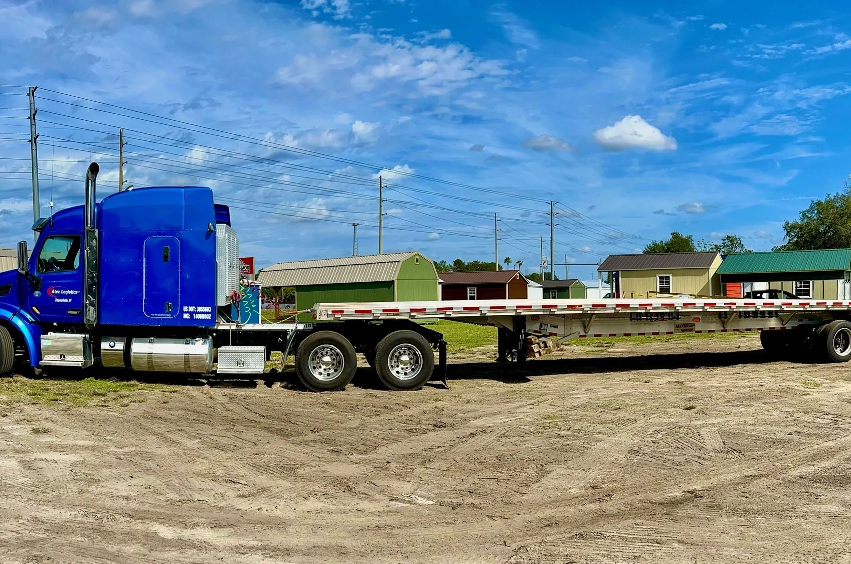 Blue semi truck with flatbed trailer on dirt ground.