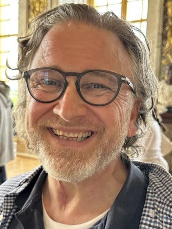Smiling man with glasses and a beard in a bright indoor setting.
