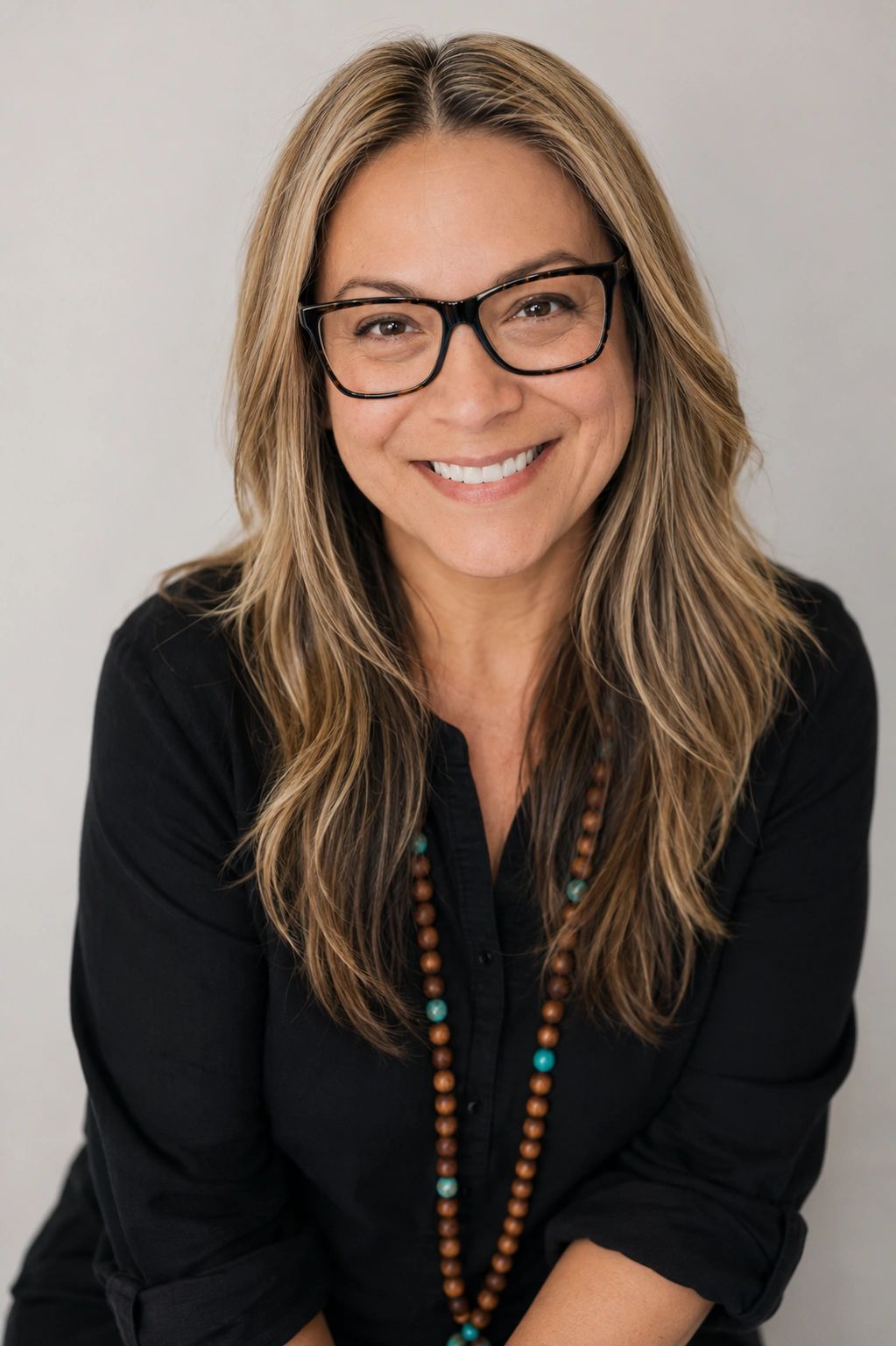 Smiling woman with glasses and a beaded necklace.