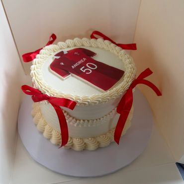 A white birthday cake decorated with red ribbons and a soccer jersey topper.