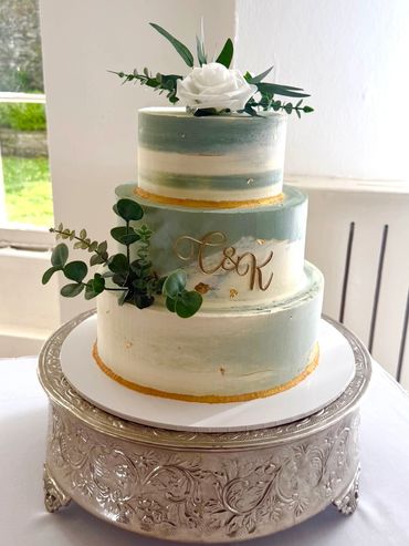 Elegant three-tiered cake with green accents and floral decoration on ornate silver stand.
