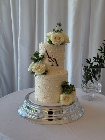 Elegant two-tier white wedding cake adorned with cream roses and greenery.