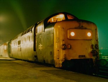 Vintage train at night with glowing headlights.