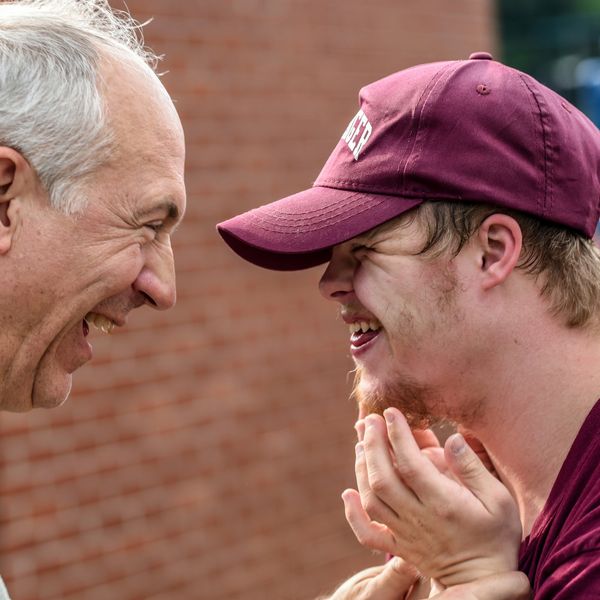 An elderly man and a young man share a joyful moment, smiling closely.