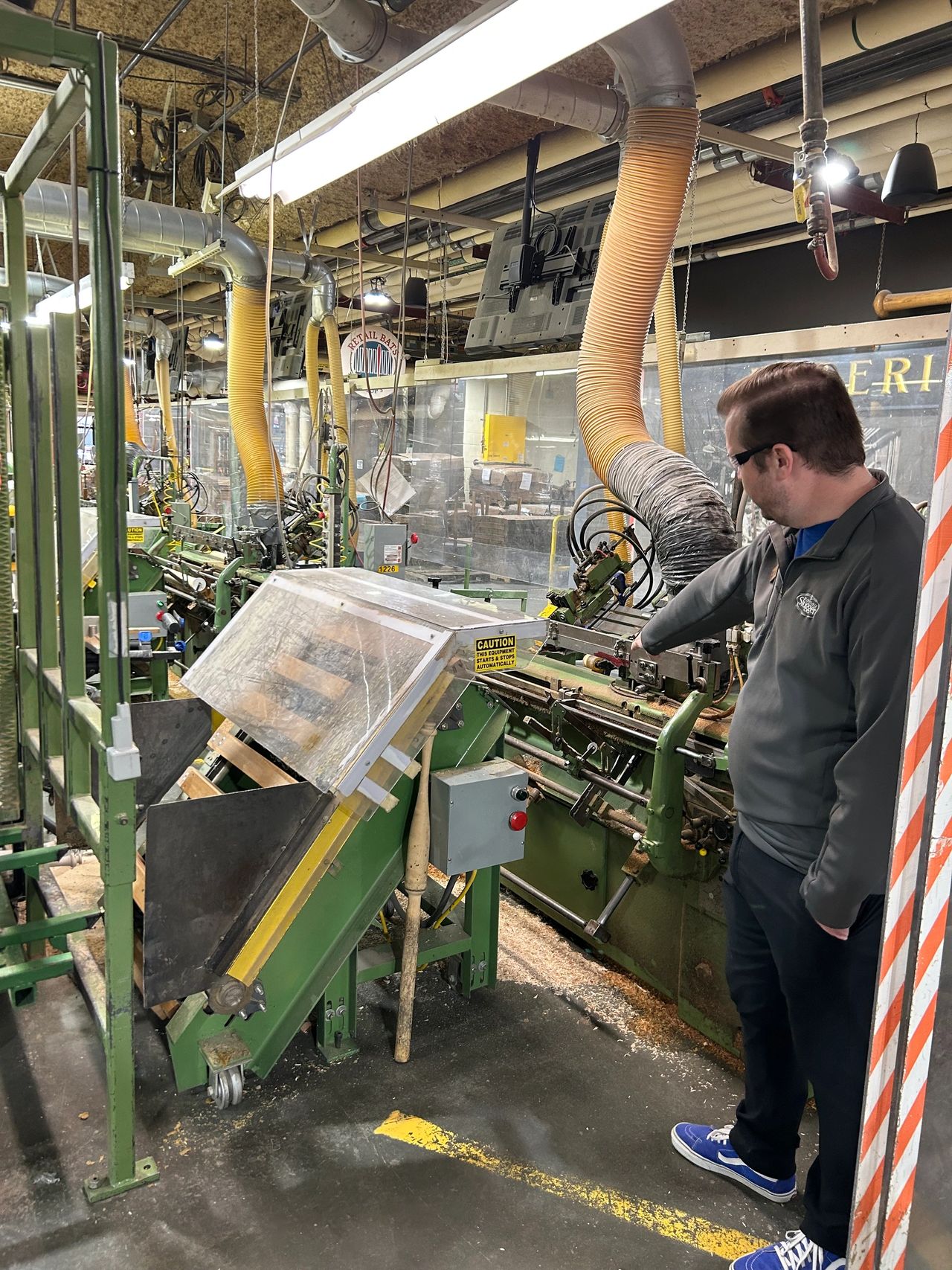 A man observing the automated lathe process as a wooden billet is shaped into a baseball bat during the Louisville Slugger factory tour.