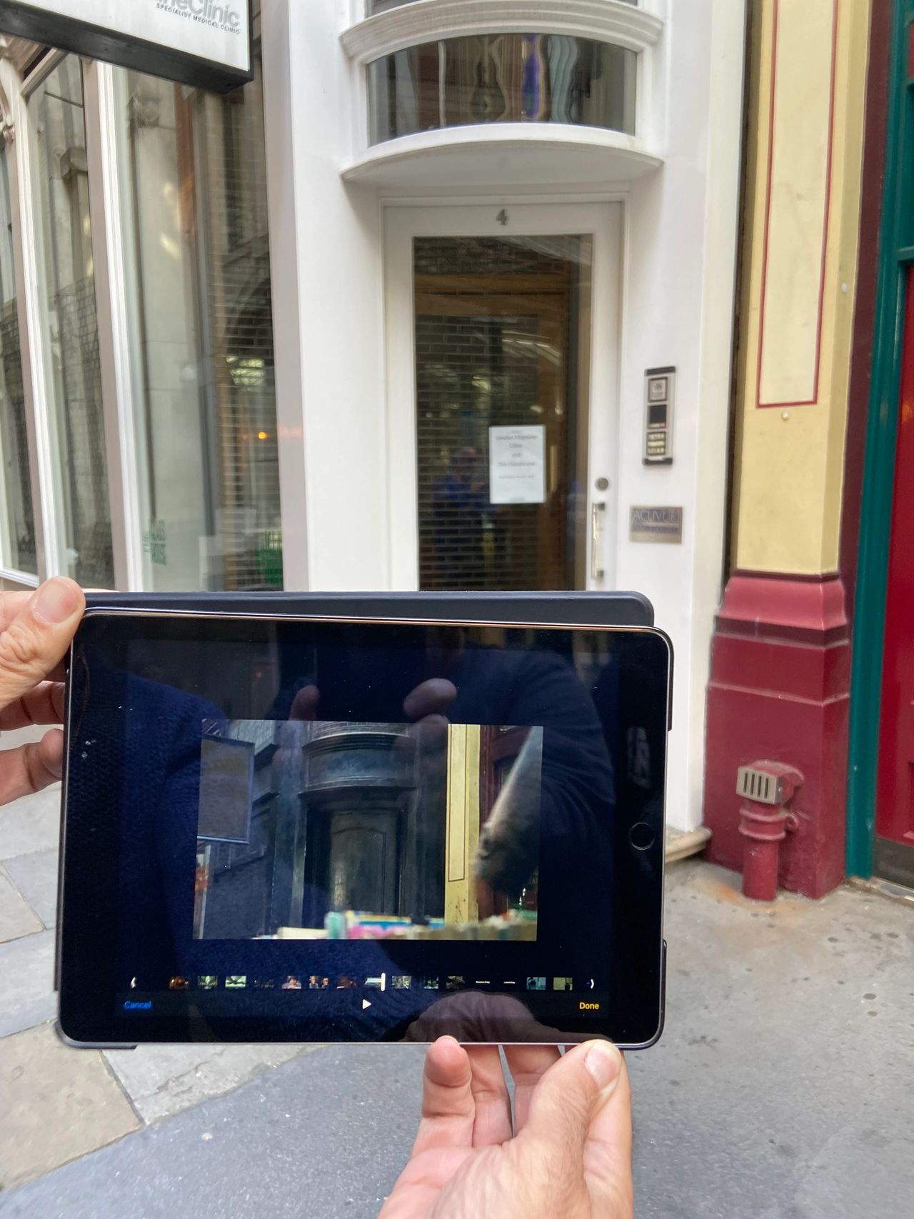 A person holding an iPad displaying a scene from Harry Potter and the Sorcerer's Stone in front of the real-life filming location at 42 Bull’s Head Passage in Leadenhall Market, London, which served as the entrance to the Leaky Cauldron.
