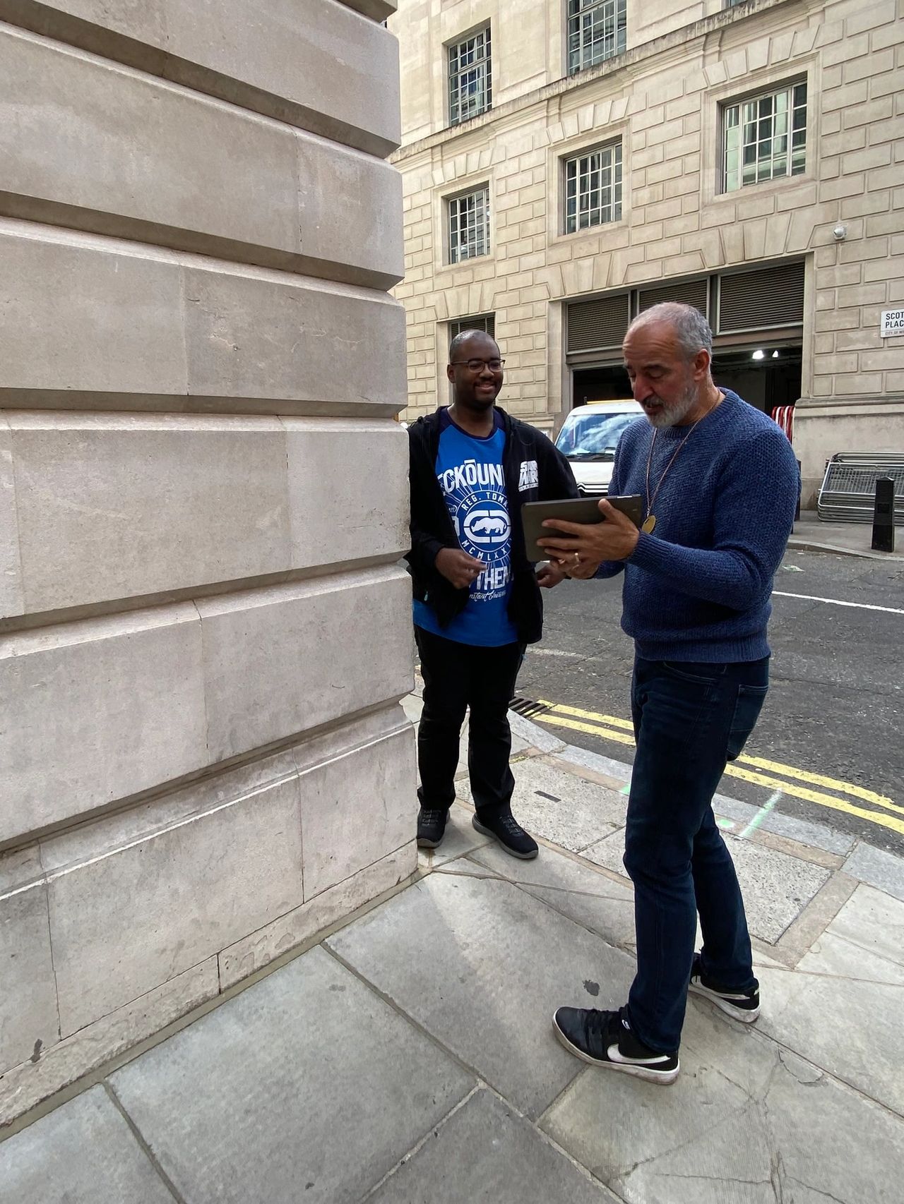 A guided stop at the Great Scotland Yard Harry Potter location where the Ministry of Magic entrance was filmed. The photo shows the black taxi driver using a digital tablet to compare the real London street to the movie scene.