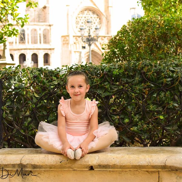 Niña con vestido de ballet rosa sentada al aire libre.