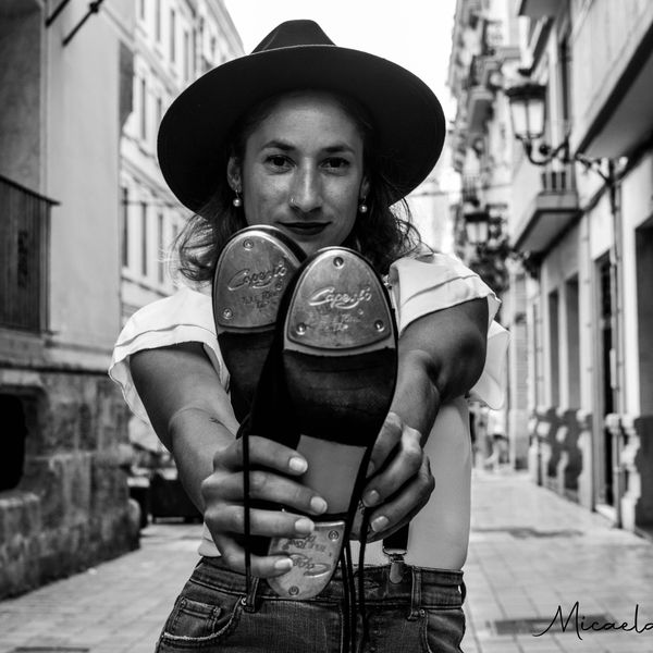 Mujer con sombrero mostrando la suela de sus zapatos en la calle.