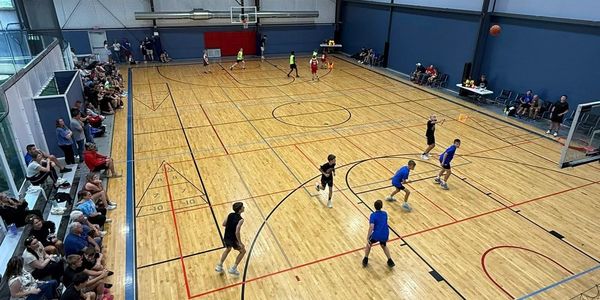 Indoor basketball game with players and a seated audience.
