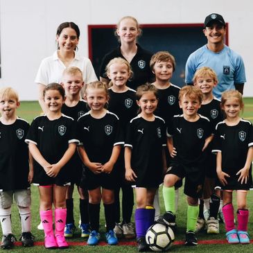 Children's soccer team posing with coaches on a field.
