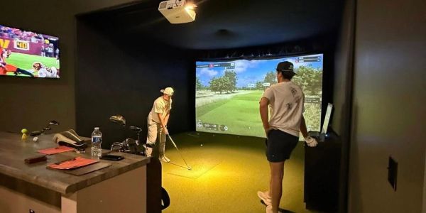 Two men playing golf in an indoor golf simulator room.