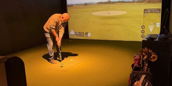 Man playing golf indoors using a golf simulator setup.