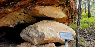 A large rock formation with a sign in a wooded area.