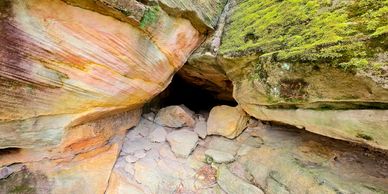 Rocky cave entrance surrounded by moss and colorful stone layers.