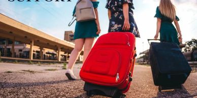Three women walking down a street with luggage.