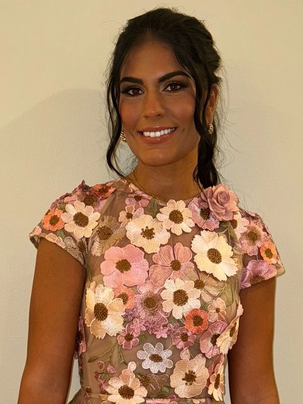 Woman in a floral embroidered dress smiling at the camera.