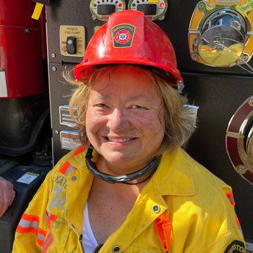 Smiling firefighter in yellow gear and red helmet.