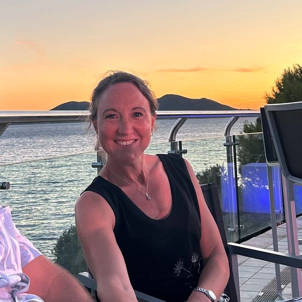 Woman smiling at sunset on a balcony by the sea.