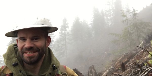 A smiling man in front of dead trees