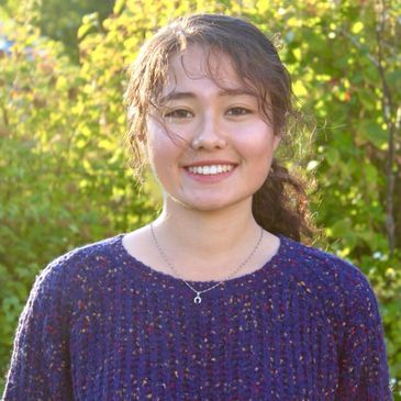 Young woman smiling outdoors with greenery background.