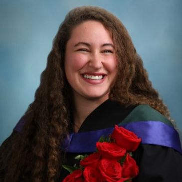Smiling graduate holding red roses in cap and gown.
