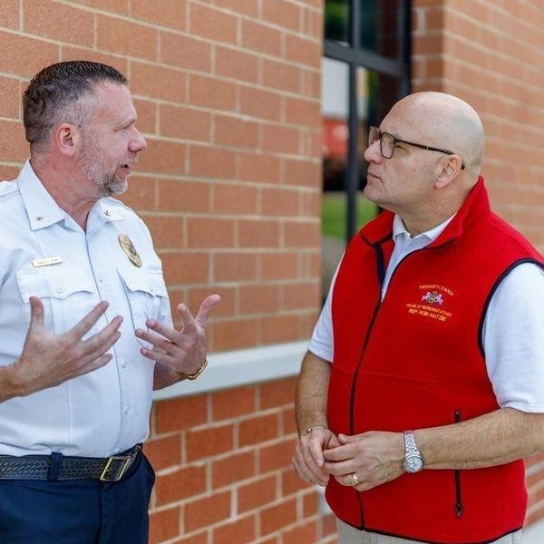 Two men conversing outside a brick building.