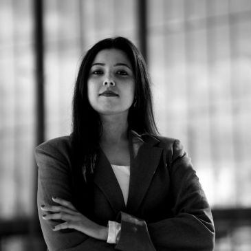 Confident woman in a blazer stands with arms crossed in a modern office.