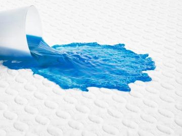 White, cooling mattress protector saves a bed surface from a blue liquid spill. 
