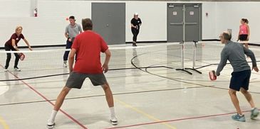 People playing pickleball indoors on a gym court.