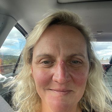 A woman with blonde hair smiling inside a car.