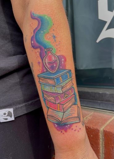 Colorful tattoo of stacked books with a magical potion bottle and cosmic smoke.