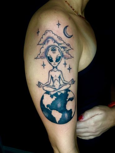 Tattoo of a meditating alien on Earth with stars and moon.