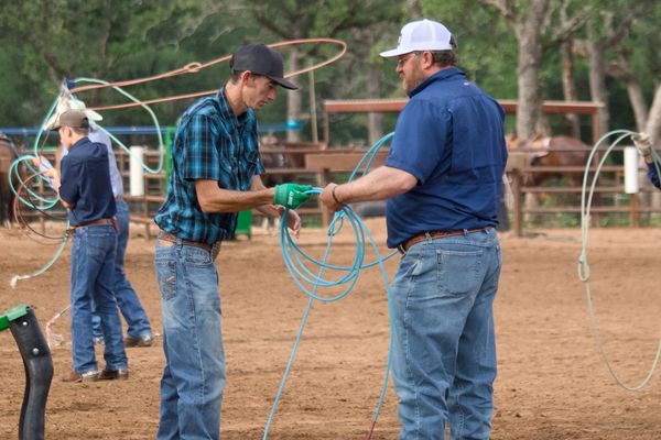 Two men practicing lasso skills in an outdoor arena.