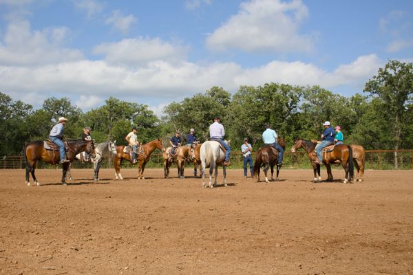 A group of people on horseback gathered in a circle in an outdoor arena.