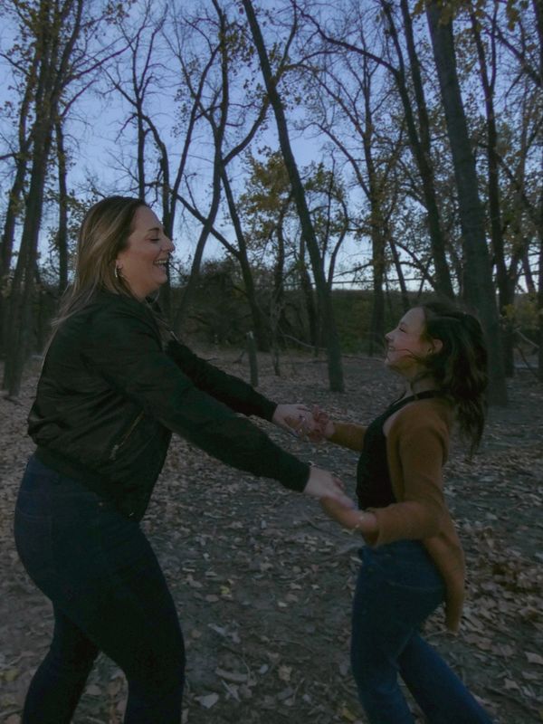 A joyful woman and girl holding hands and spinning in a forest during autumn.