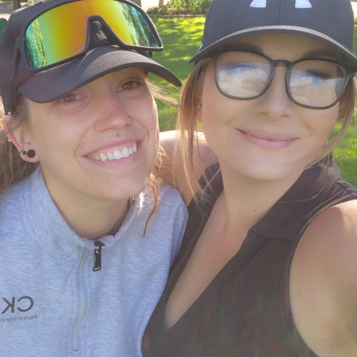 Two women smiling outdoors, wearing hats and casual clothes.