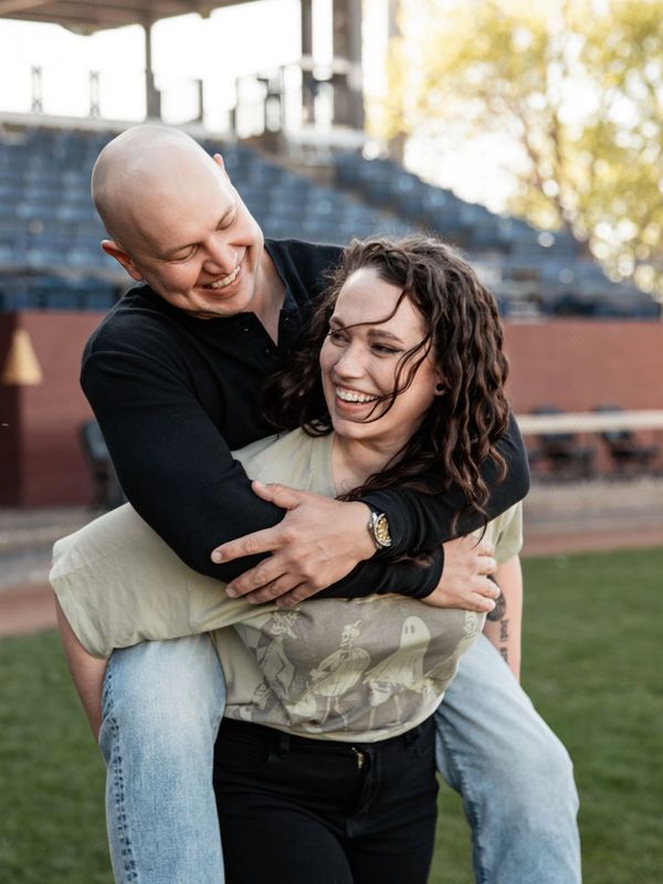 Happy couple enjoying a playful piggyback moment outdoors at a sports field.