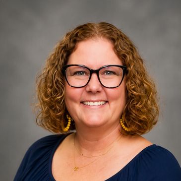 Smiling woman with curly hair and glasses.