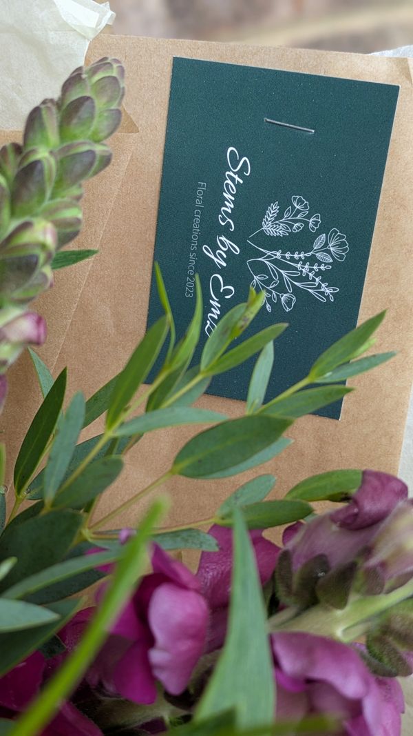 Floral arrangement with a 'Stems by Emi' card on brown wrapping paper.