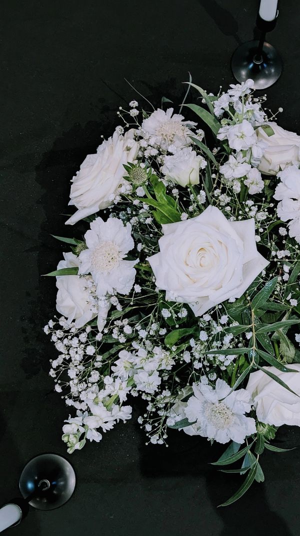 Elegant white floral arrangement on a dark surface with candle holders.