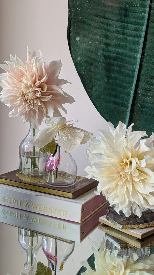 Elegant floral arrangement on books with a reflective surface and large green leaf backdrop.