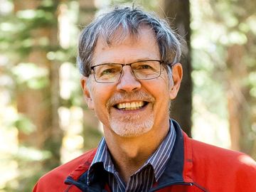 Smiling older man with glasses outdoors.
